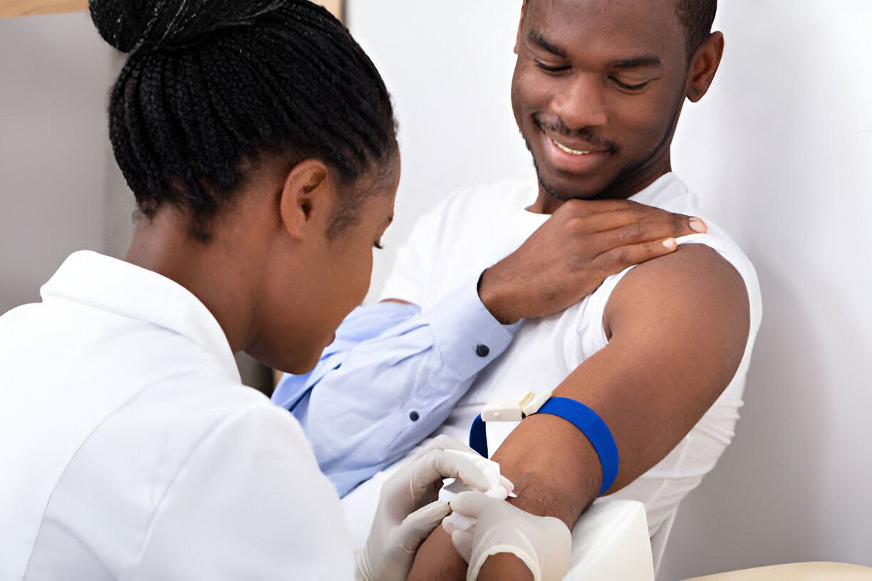 A phlebotomist drawing blood from a seated patient's arm with a tourniquet in place